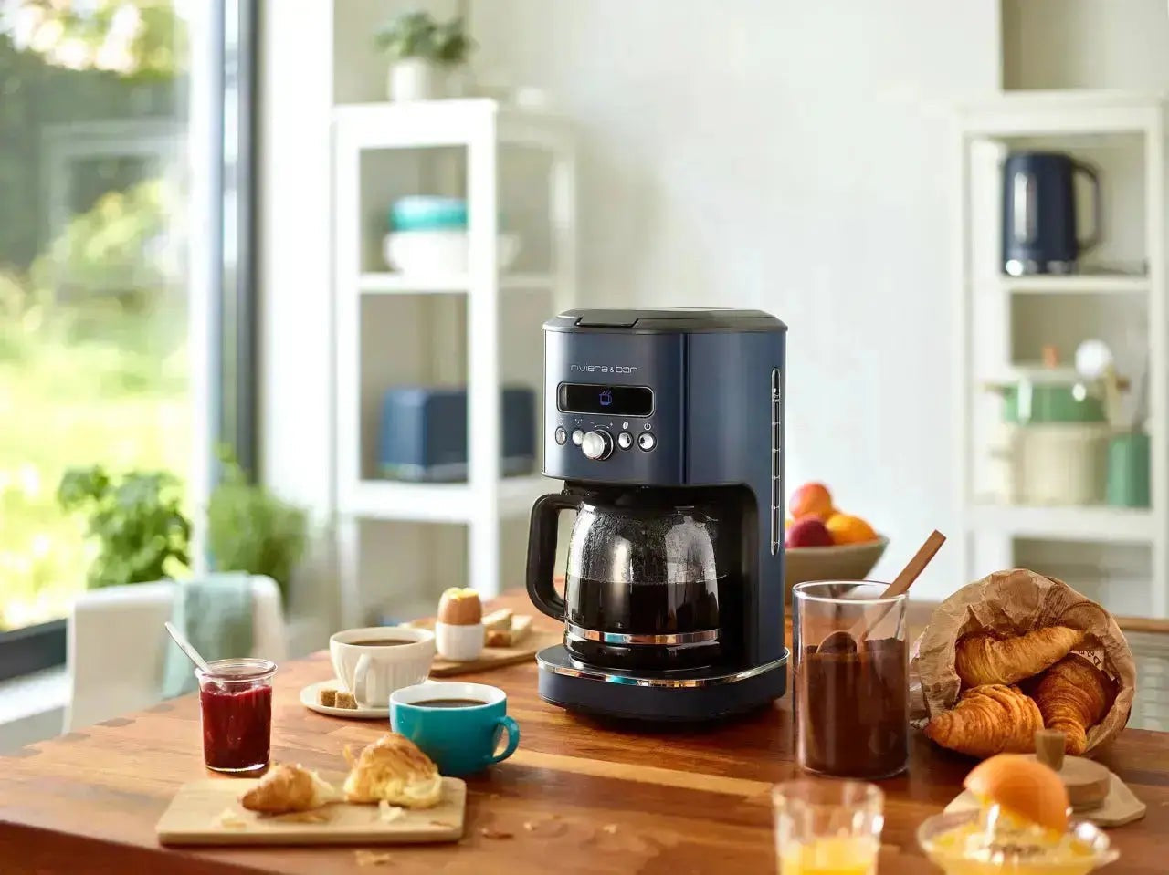 Blauw koffiezetapparaat op houten tafel met ontbijt.
