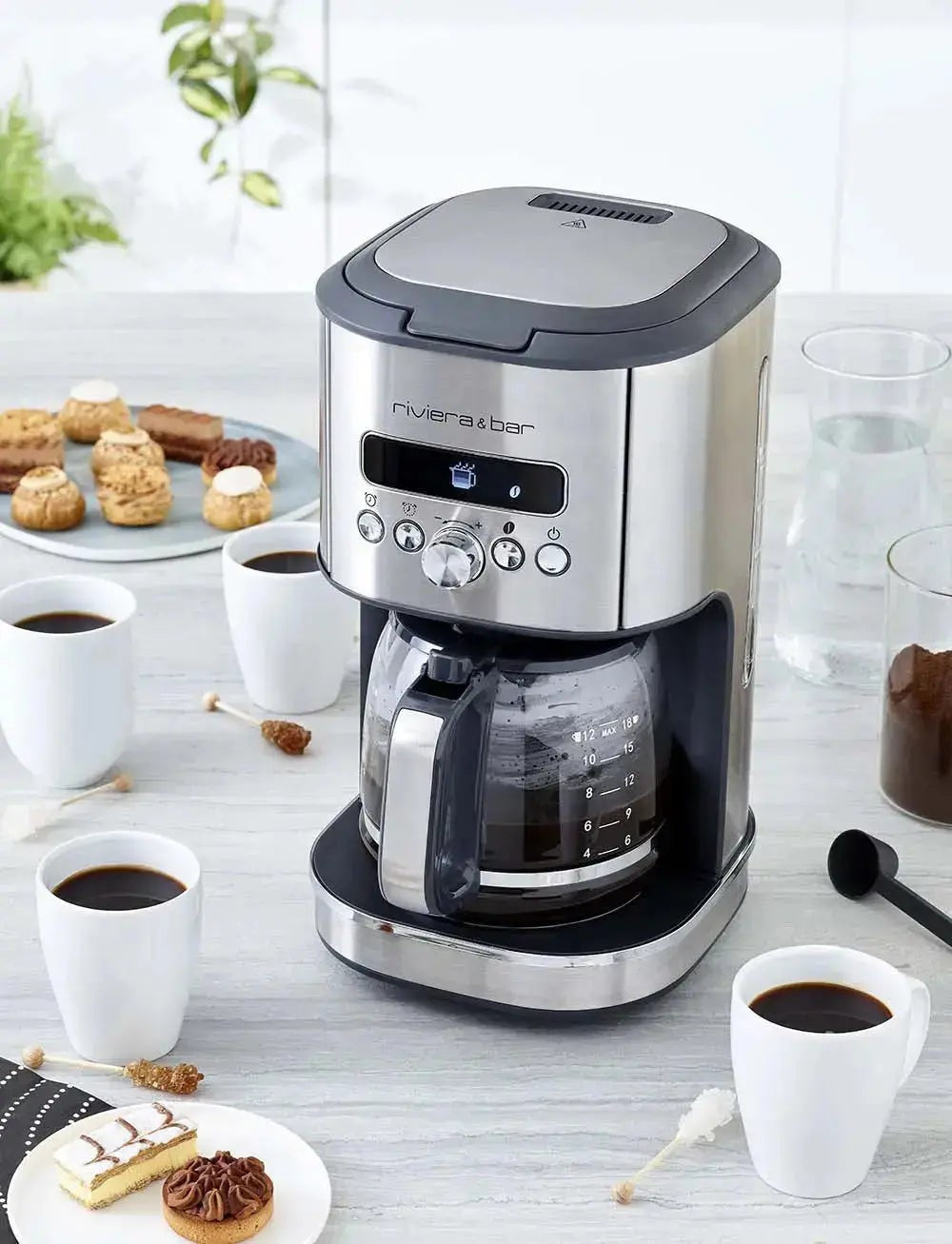 Koffiezetapparaat Riviera & Bar van roestvrij staal, koffiekopjes en gebak.