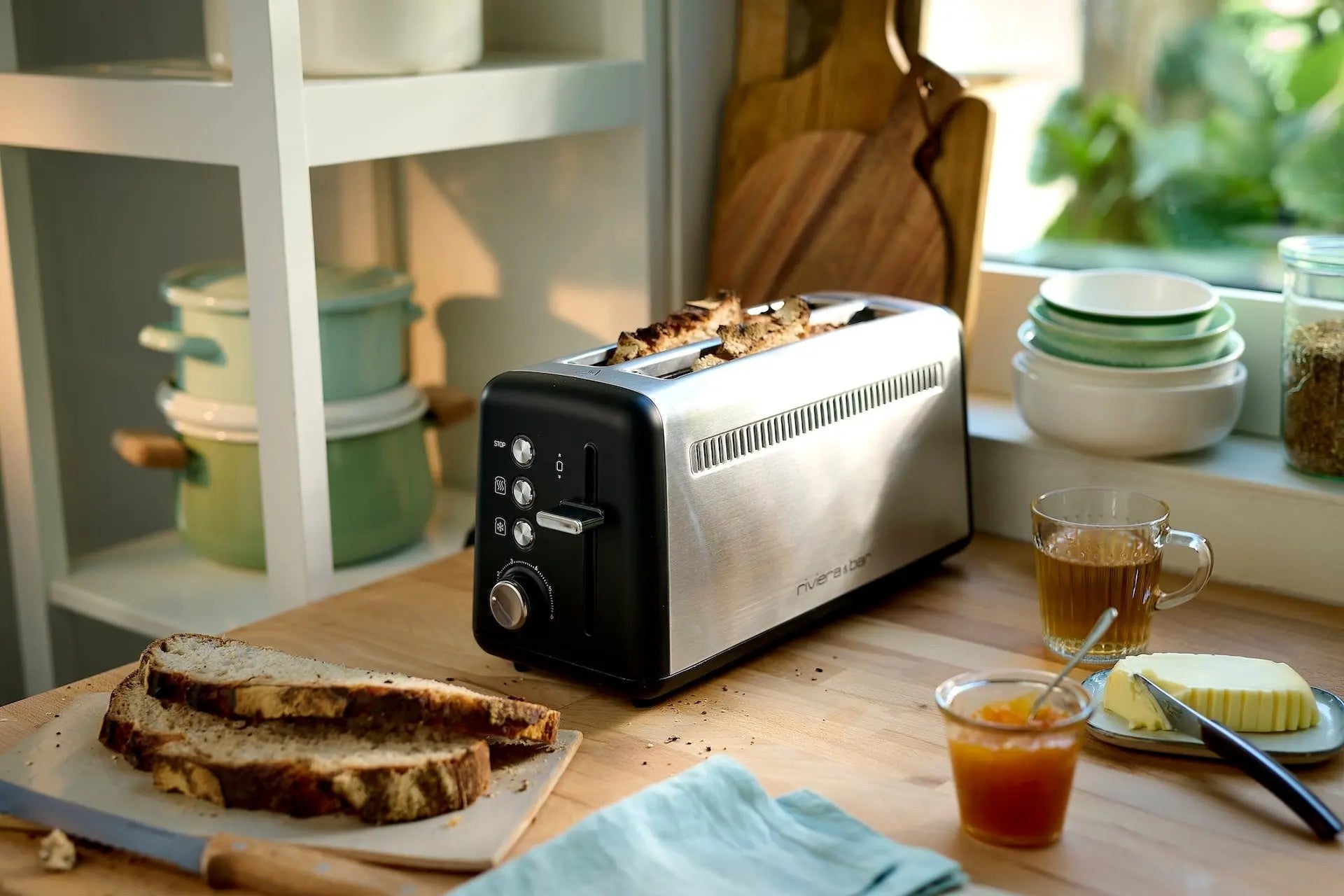 Zwart en zilverkleurig broodrooster, toast, thee, jam, boter, lichte binnenkant.