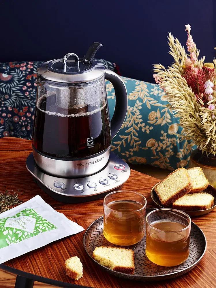 Elektrische theepot met thee, kopjes en cake.